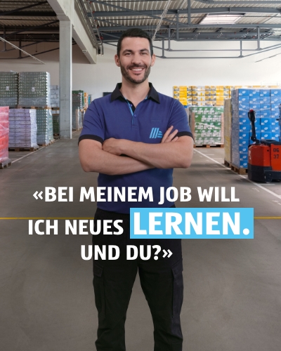 Mann steht in einem Lager und lächelt freundlich. Im Hintergrund sind Paletten mit Produkten sichtbar. Auf der Bildüberschrift steht: Bei meinem Job will ich neues Lernen. Und du?