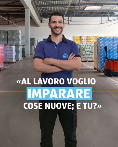 Un uomo si trova in un magazzino e sorride amichevolmente. Sullo sfondo sono visibili i pallet con i prodotti. La didascalia della foto recita: al lavoro voglio imparare cose nuove. E tu?
