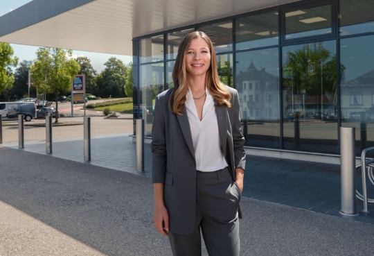 Eine Frau steht vor einer ALDI Suisse Filiale und lächelt.