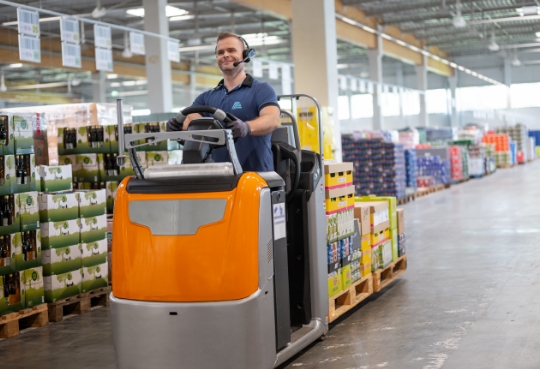 Ein Mitarbeiter fährt mit einem Stapelfahrzeug durch das Lager von ALDI Suisse.