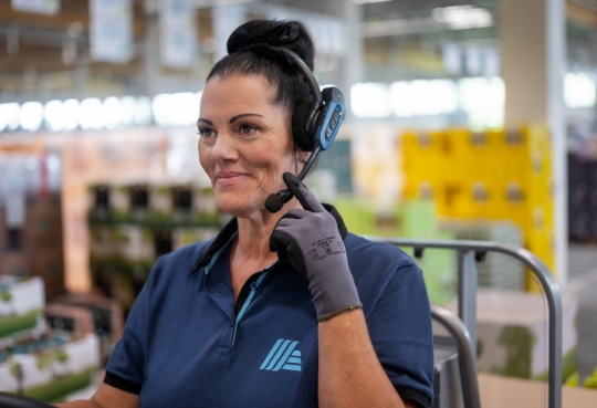 Eine Mitarbeiterin telefoniert über ihr Headset mit einer Teamkollegin im Lager.