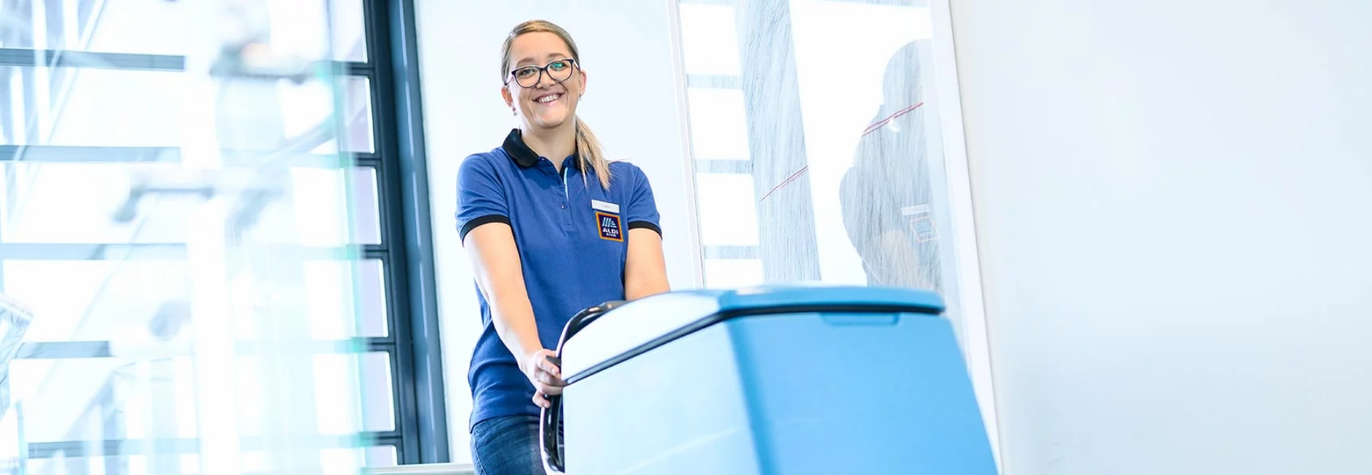 Une femme souriante nettoie le sol avec un appareil de nettoyage.