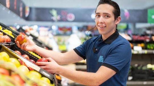 Ein ALDI Suisse Mitarbeiter prüft Äpfel in den Regalen auf Qualität.