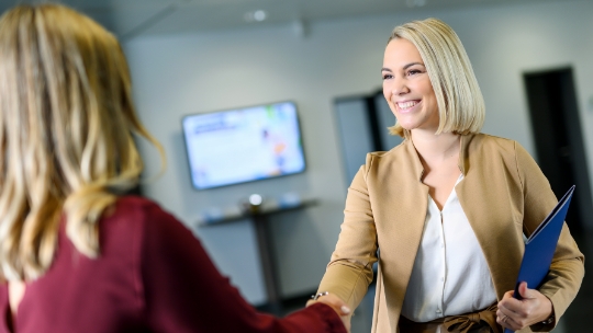 Une femme accueille une autre femme en souriant pour un entretien d'embauche.