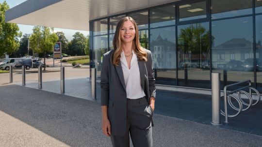Une femme se tient devant une filiale d'ALDI Suisse et sourit.