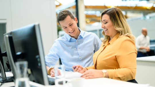 Un homme et une femme se tiennent devant un bureau debout et regardent ensemble un document.