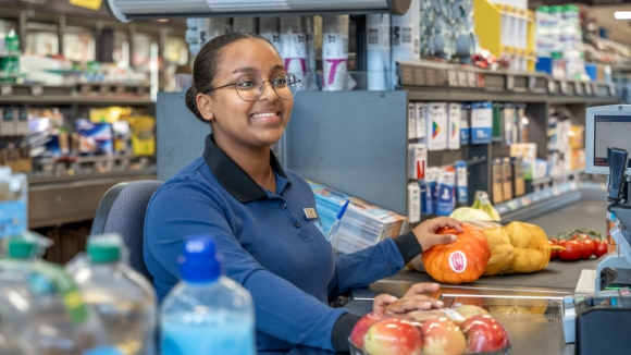 Dans la filiale ALDI Suisse, une collaboratrice se tient devant le rayon légumes et sourit.