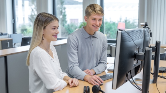 Une jeune femme et un jeune homme sont au travail et discutent ensemble de quelque chose devant le bureau.