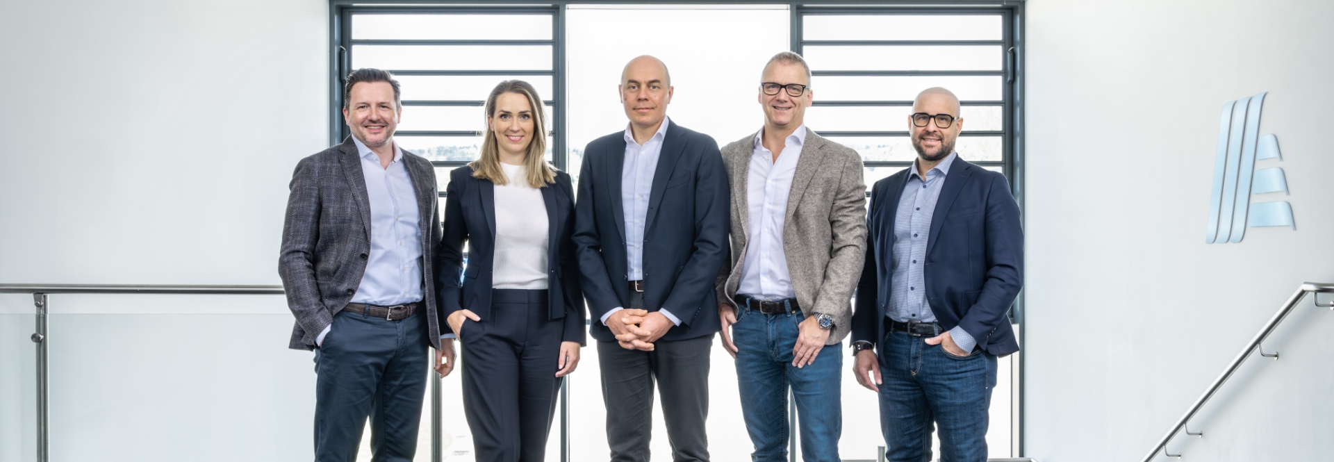 Un gruppo di persone, composto da una donna e tre uomini, che compongono la direzione di ALDI Suisse, si trovano l'una accanto all'altra sorridendo.